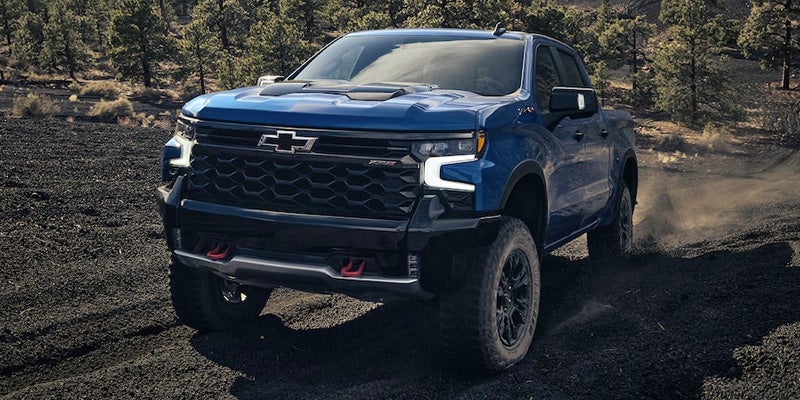 Image of a blue 2022 Chevrolet Silverado 1500 driving in the woods with dust behind